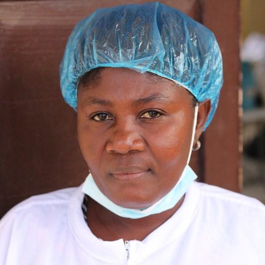 Ficienne heeft haar plastic muts op en een mondkapje naar beneden als zij vertelt over de training van ActionAid