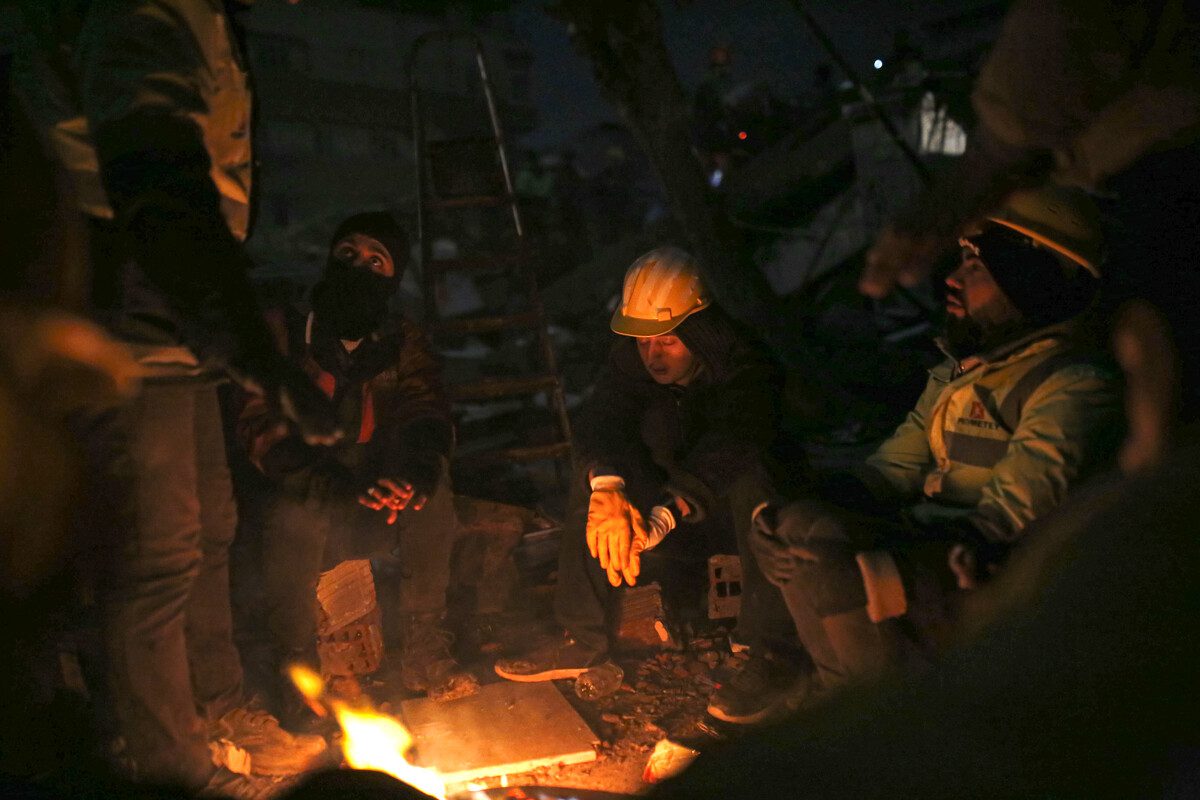 De reddingswerkers zitten uitgeput rond een vuurtje om even bij te komen.