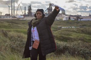 Khosi staat met vuist omhoog vóór de Tata fabriek.