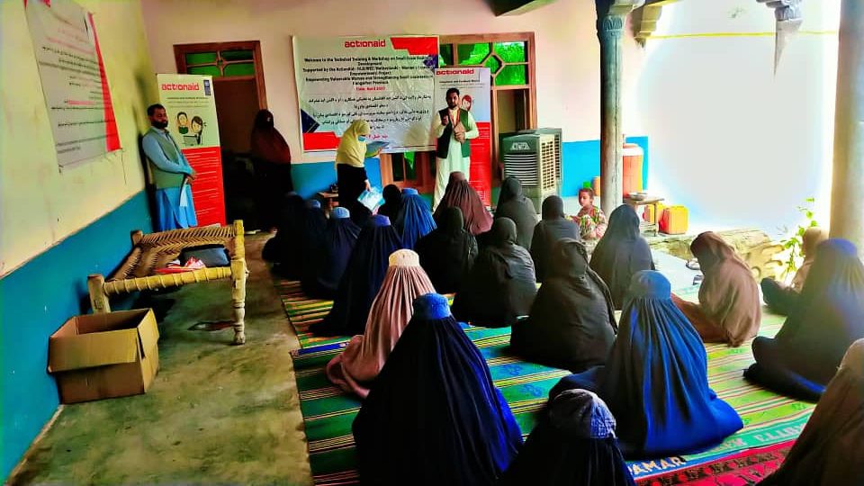 Een groep vrouwen in boerkas zit op de grond te luisteren naar een instructeur terwijl een dame papieren uitdeelt.
